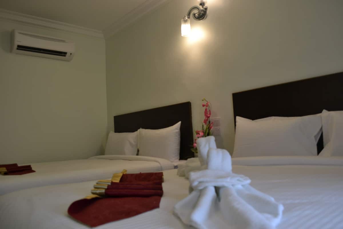 Habitación de hotel con dos camas, ropa de cama blanca, cabecera, aire acondicionado y lámpara fijada a la pared.