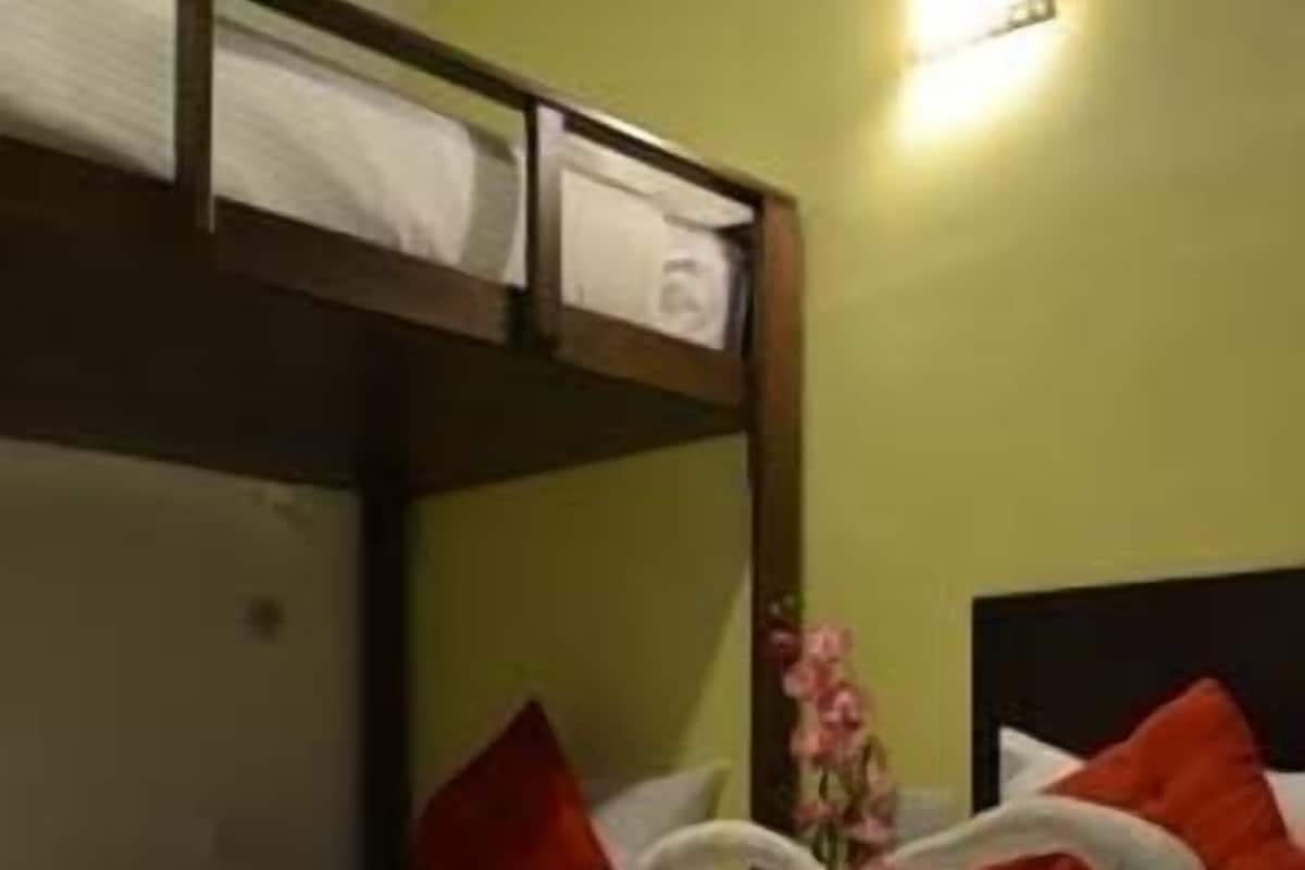 Una habitación de hotel con una cama litera, una colcha roja y un ramo de flores.