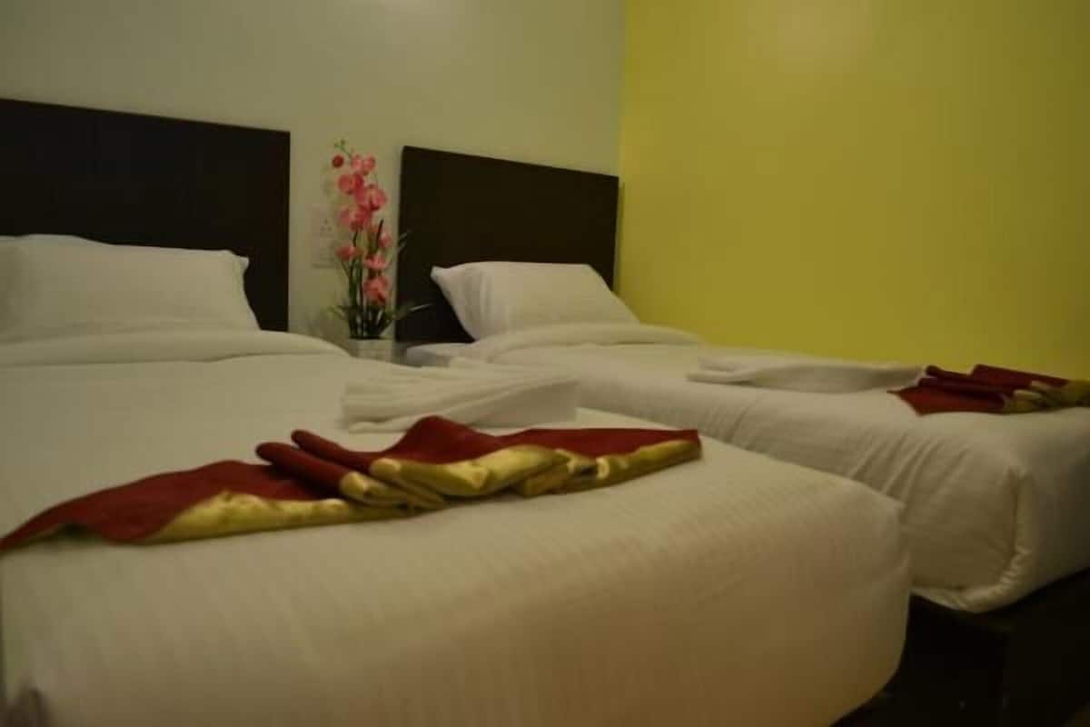 Una habitación de hotel con dos camas, ropa blanca y un jarrón con flores rosadas.