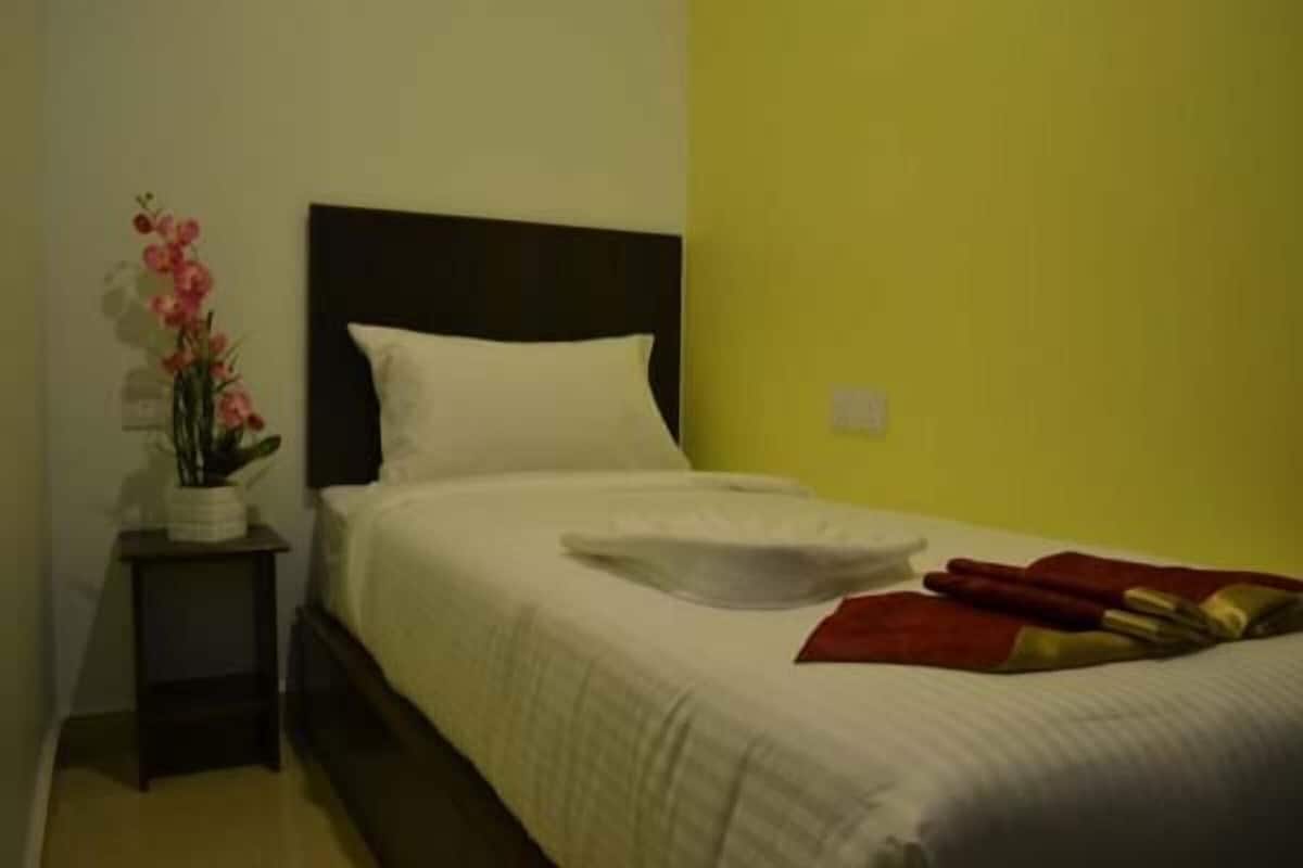 Una habitación de hotel con una cama, una mesita de noche con una planta y una pared amarilla.