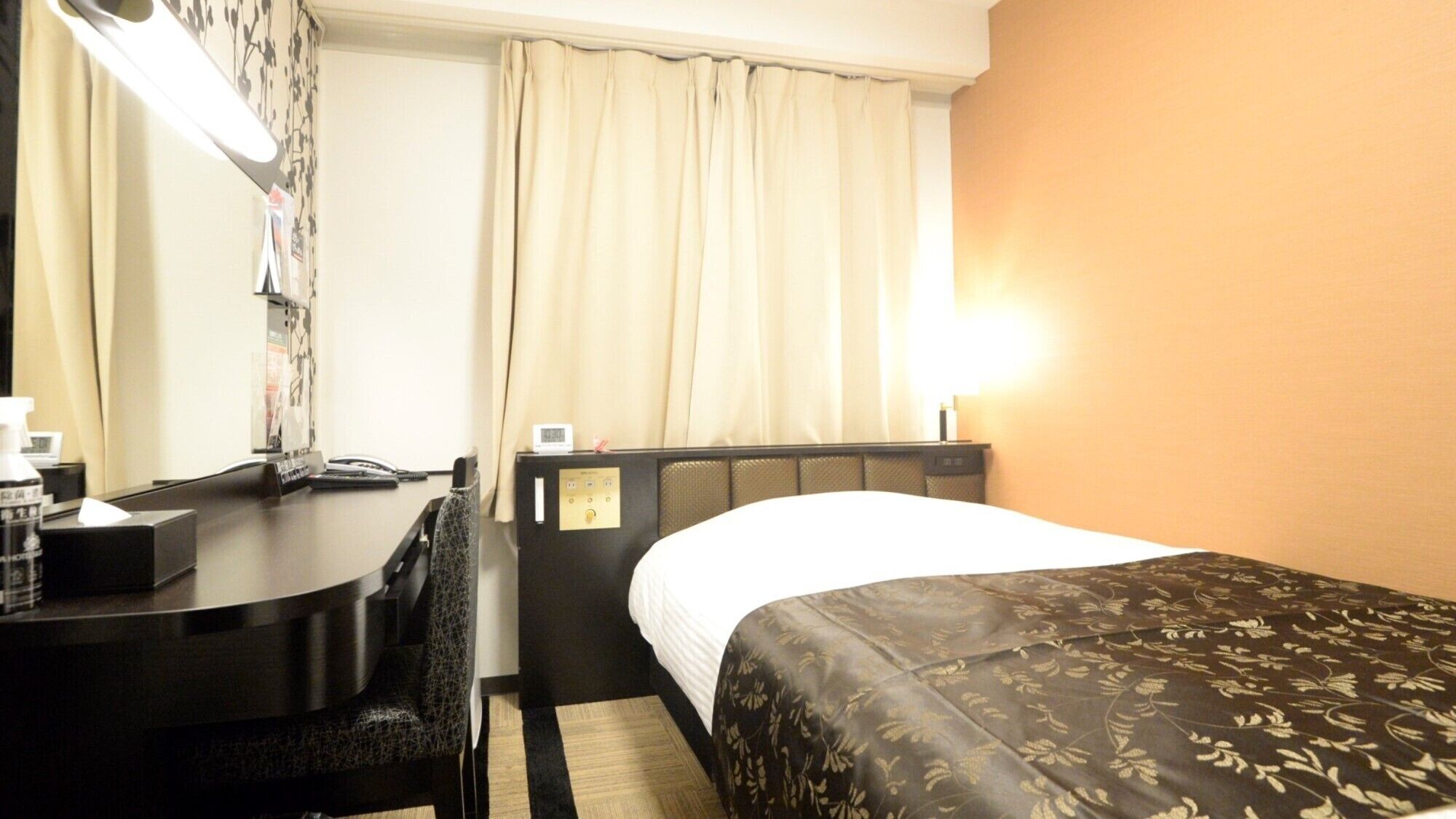 Habitación de hotel con cama, escritorio, teléfono, silla, mesita de noche y lámpara.