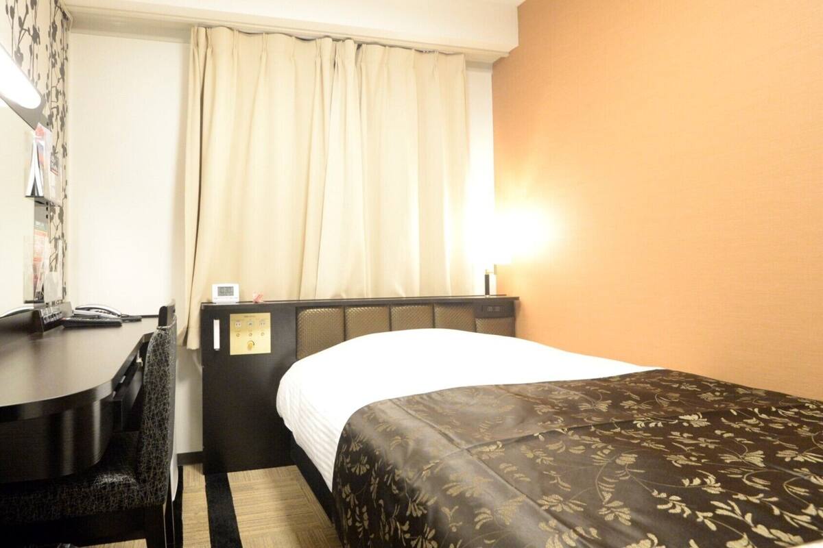 Habitación de hotel con cama, escritorio, teléfono, silla, mesita de noche y lámpara.