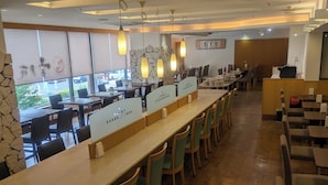 Een restaurantinterieur met lange gedeelde tafels, afgeschermde zithoeken en een accentmuur van steen.