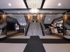 Un moderno vestíbulo de hotel con una escalera central, paredes de vidrio y un techo con diseño.