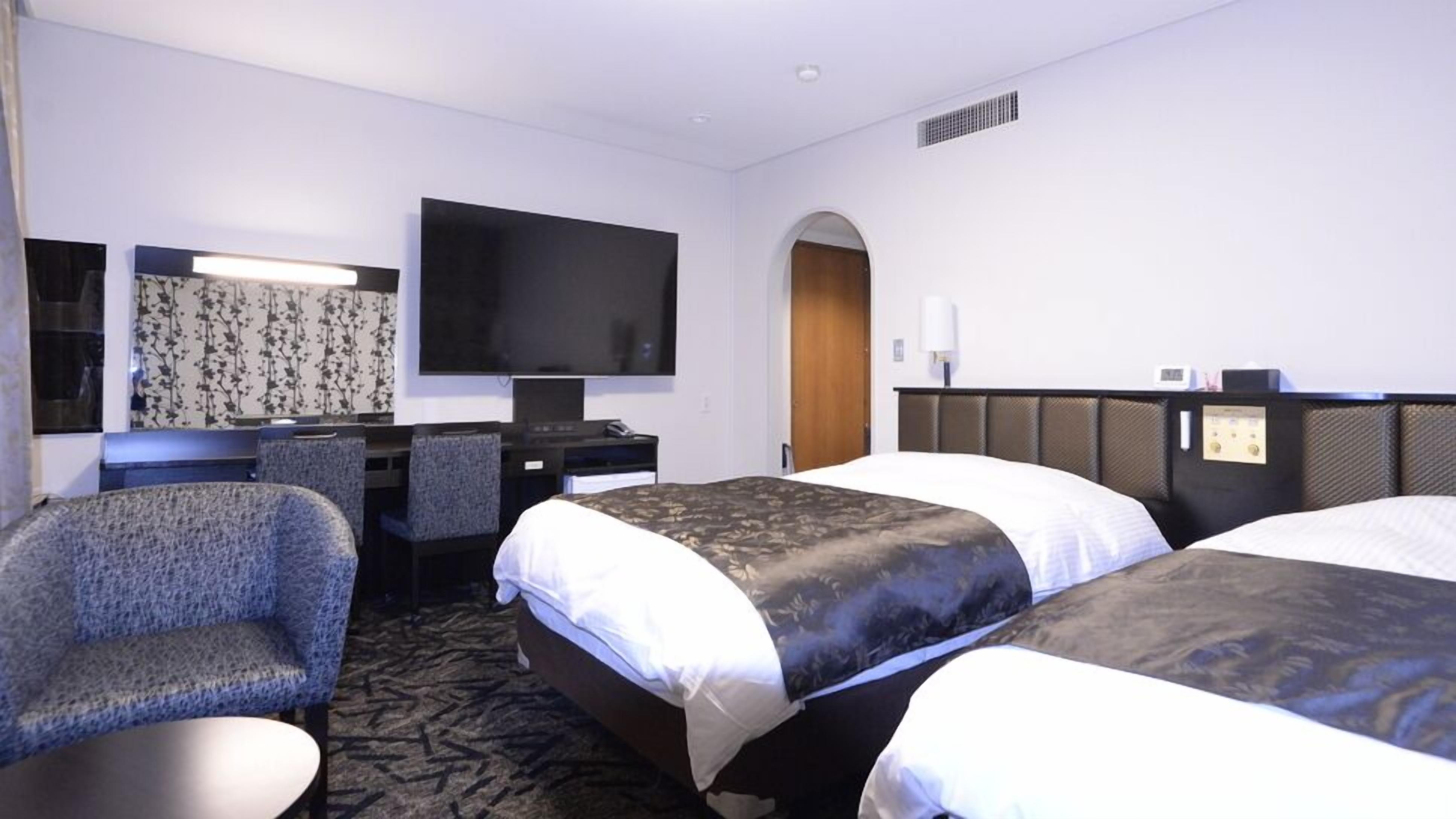 Habitación de hotel con dos camas, un escritorio, una silla, un televisor y zona de ducha.