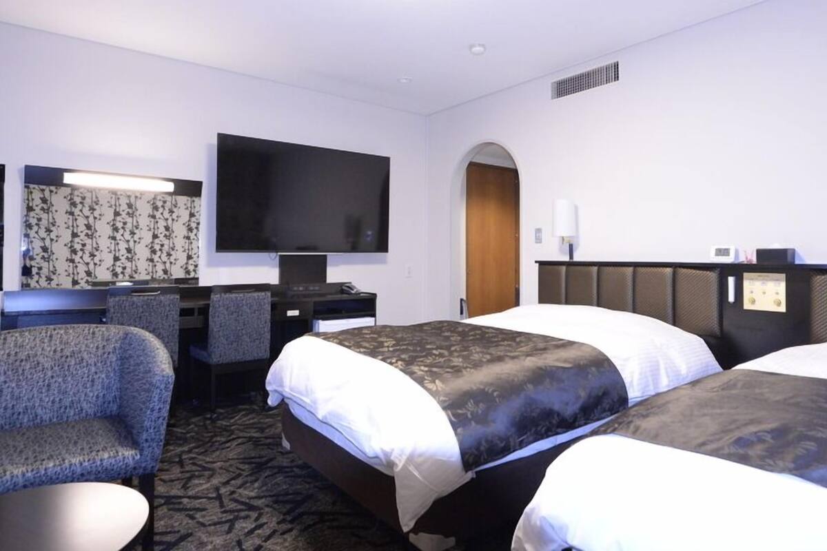 Habitación de hotel con dos camas, un escritorio, una silla, un televisor y zona de ducha.