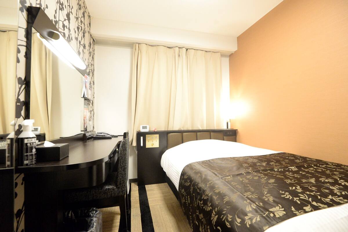 Una habitación de hotel con cama, escritorio, silla, lámpara y mesita de noche.