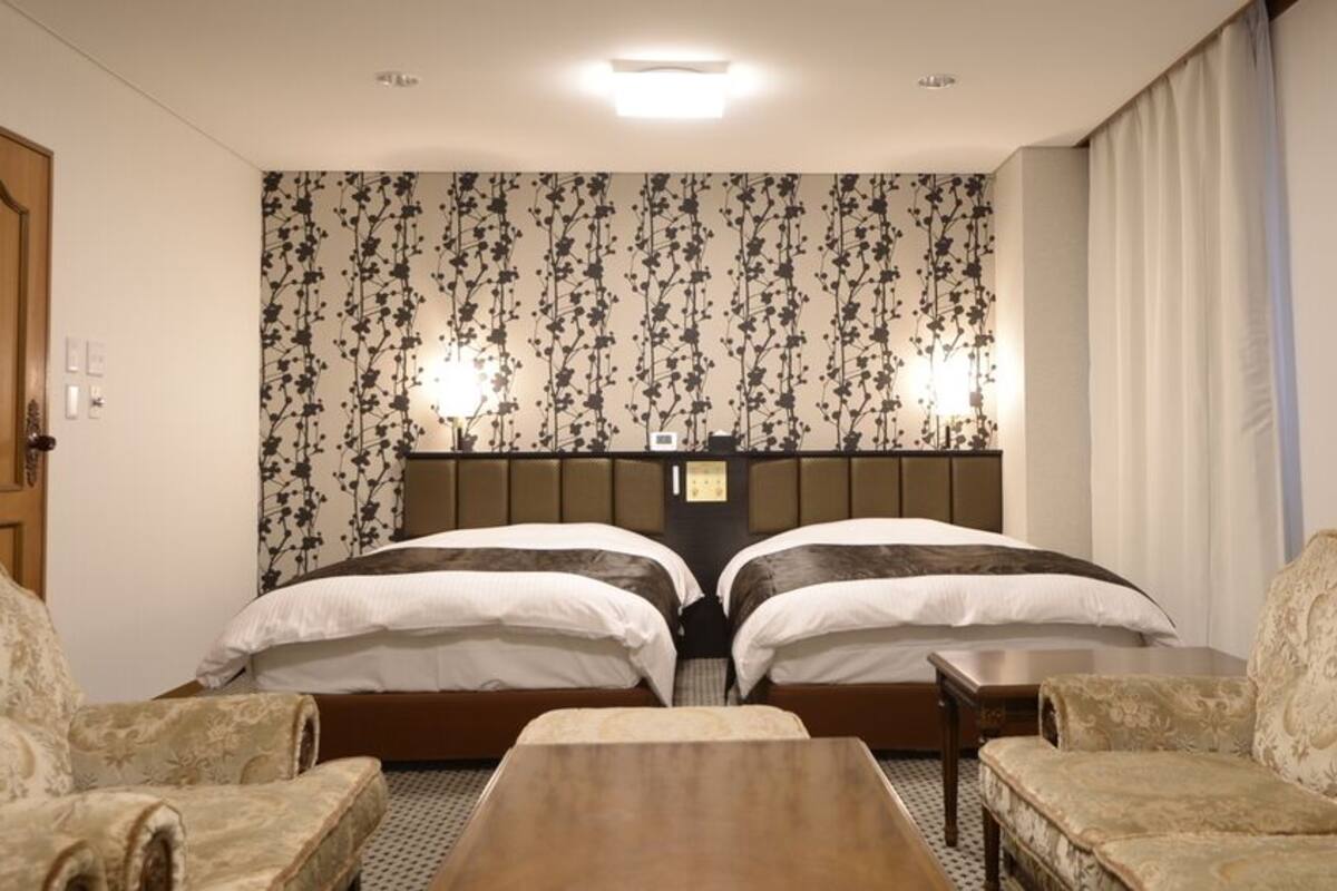 Una habitación de hotel con dos camas, una puerta de madera, un papel tapiz estampado y una pequeña mesa.