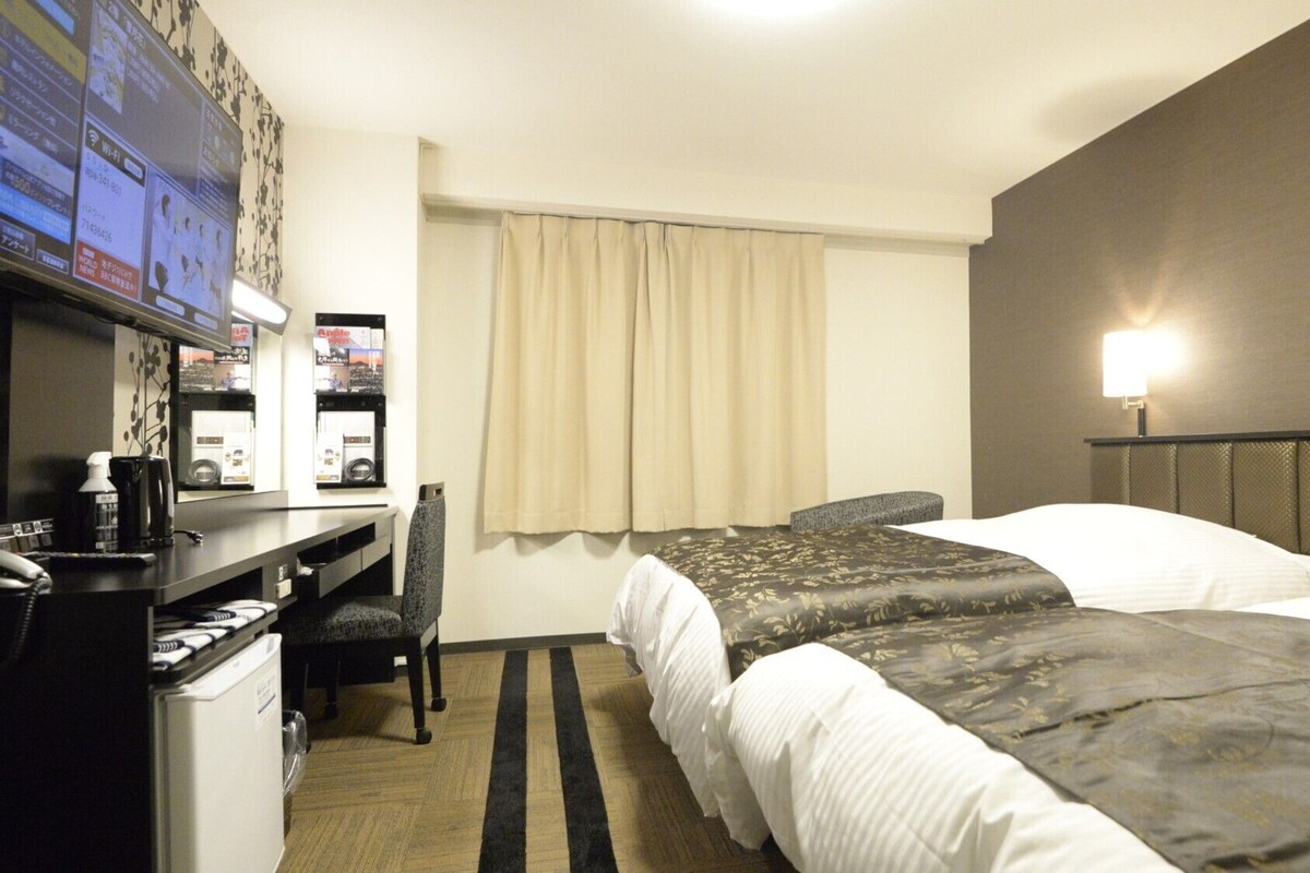 Une chambre d’hôtel avec deux lits, un bureau avec une chaise, une télévision et un minibar.