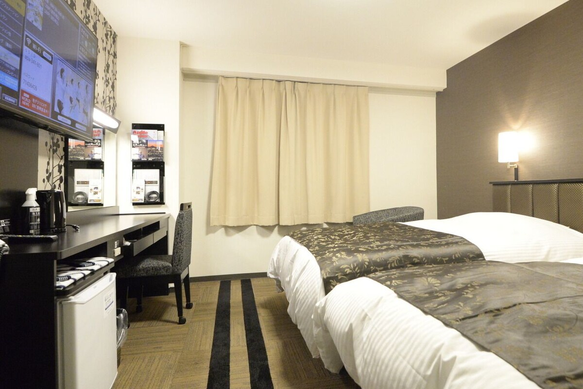 Une chambre d’hôtel avec deux lits, un bureau avec un ordinateur, une chaise, une télévision et une lampe.