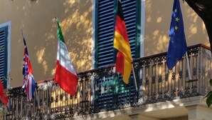 En bygning med balkon, hvor der blafres med flere flag, heriblandt EU-flaget. Indgangen har et skilt med teksten "Alberg Roma".