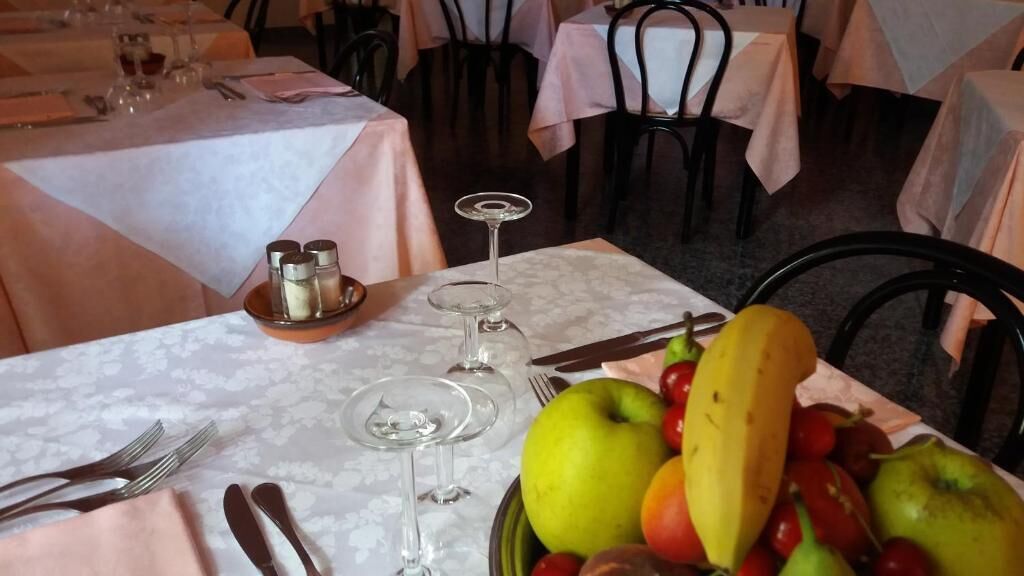 Una mesa de comedor lista, con cubiertos, copas de vino y un frutero.