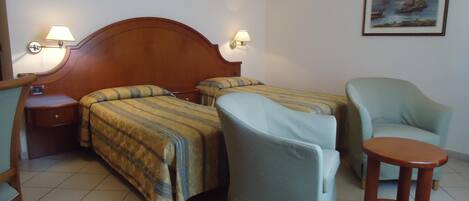 Habitación de hotel con dos camas, una silla, una mesita y un cuadro en la pared.