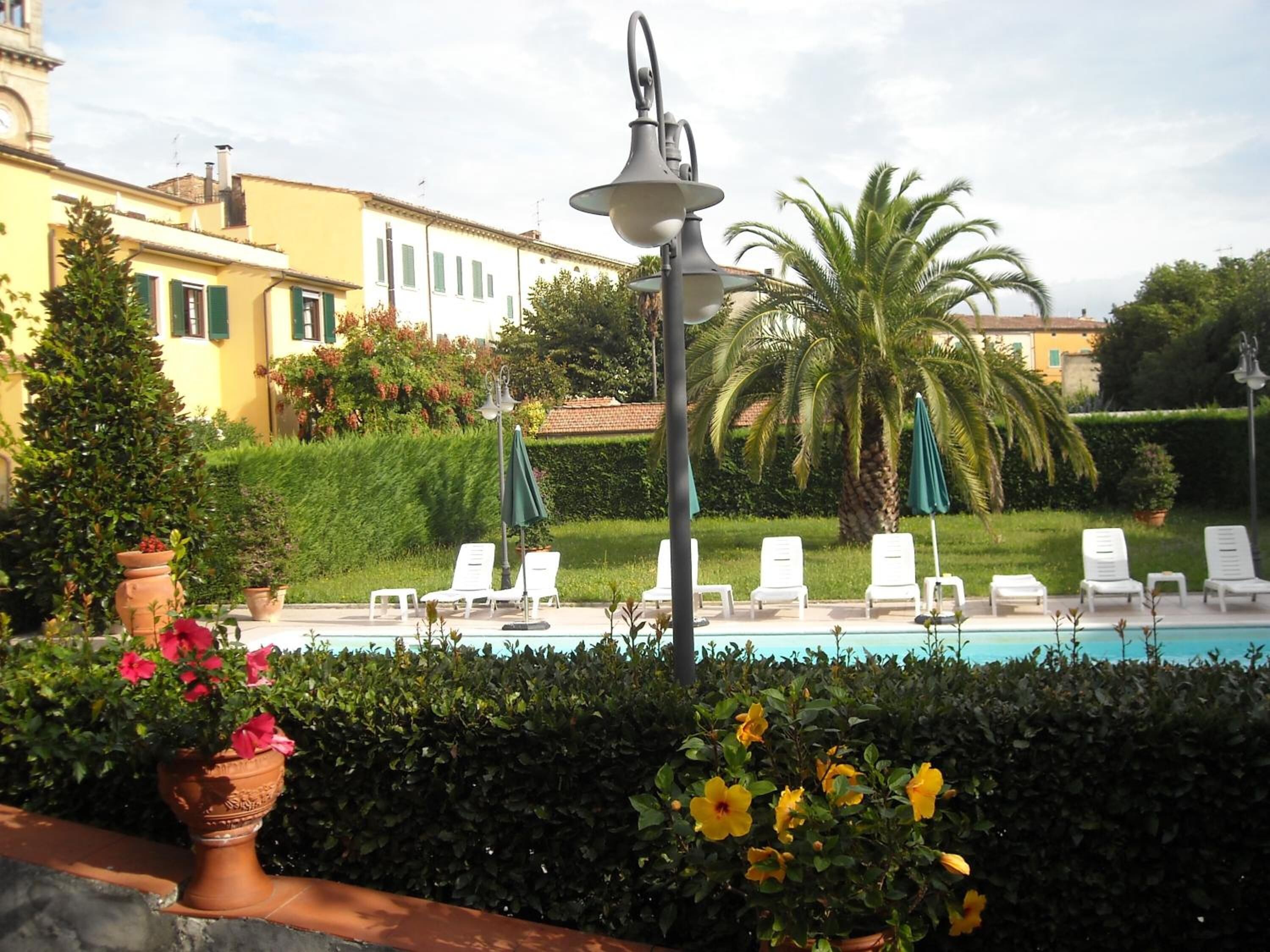 A poolside area with lounge chairs, a lamp post, and a hedge.