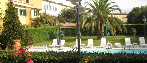 A poolside area with lounge chairs, a lamp post, and a hedge.