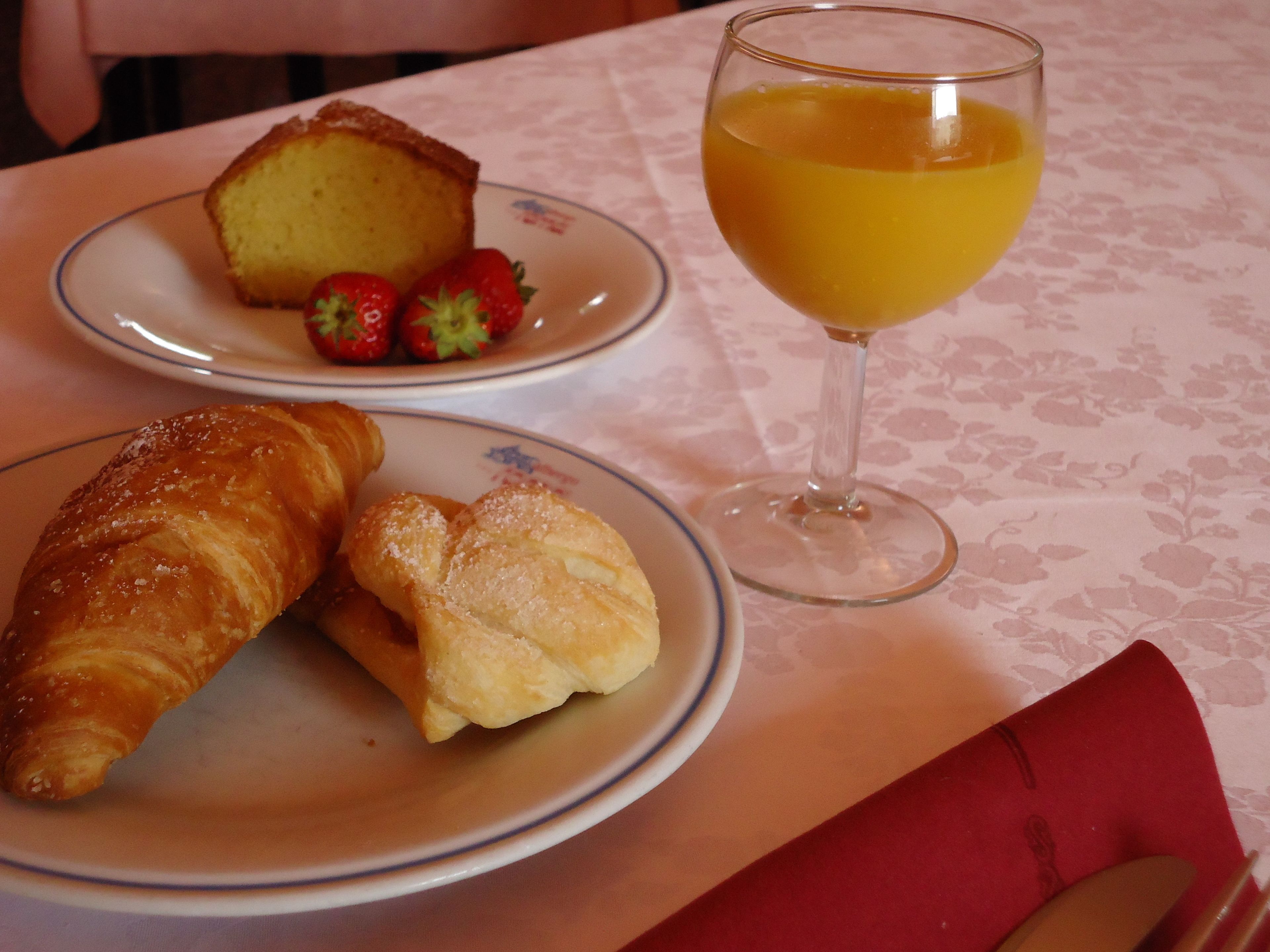 A table with plates of food including a croissant, a pastry, and strawberries, and a glass of orange juice.