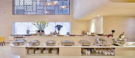 A buffet setup with multiple serving stations, a decorative partition, and a large window with natural light.