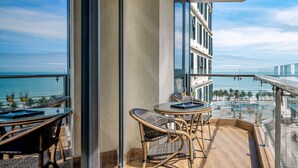 Een balkon met rieten stoelen en een tafel, met uitzicht op een strand en een stadsbeeld.
