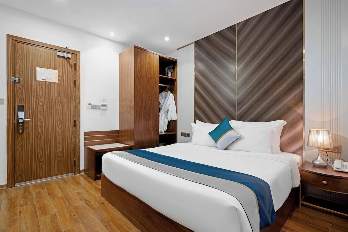 Une chambre d’hôtel avec une armoire en bois, un lit avec une literie blanche agrémentée d’une touche de bleu, une table de chevet avec une lampe et un mur orné d’un motif en chevrons.