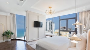 Quarto de hotel moderno com uma cama grande, televisão e vista para a cidade e para o mar.