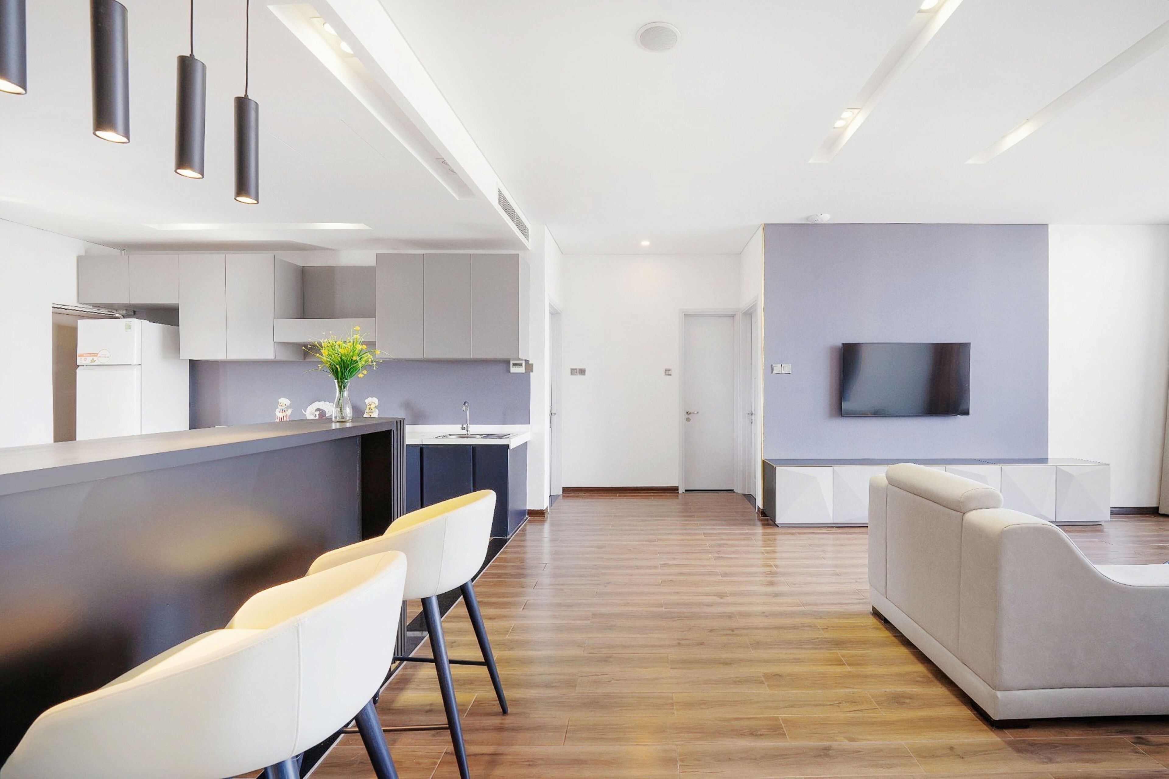 A modern kitchen with a central island, bar stools, and a flat-screen TV mounted on the wall.