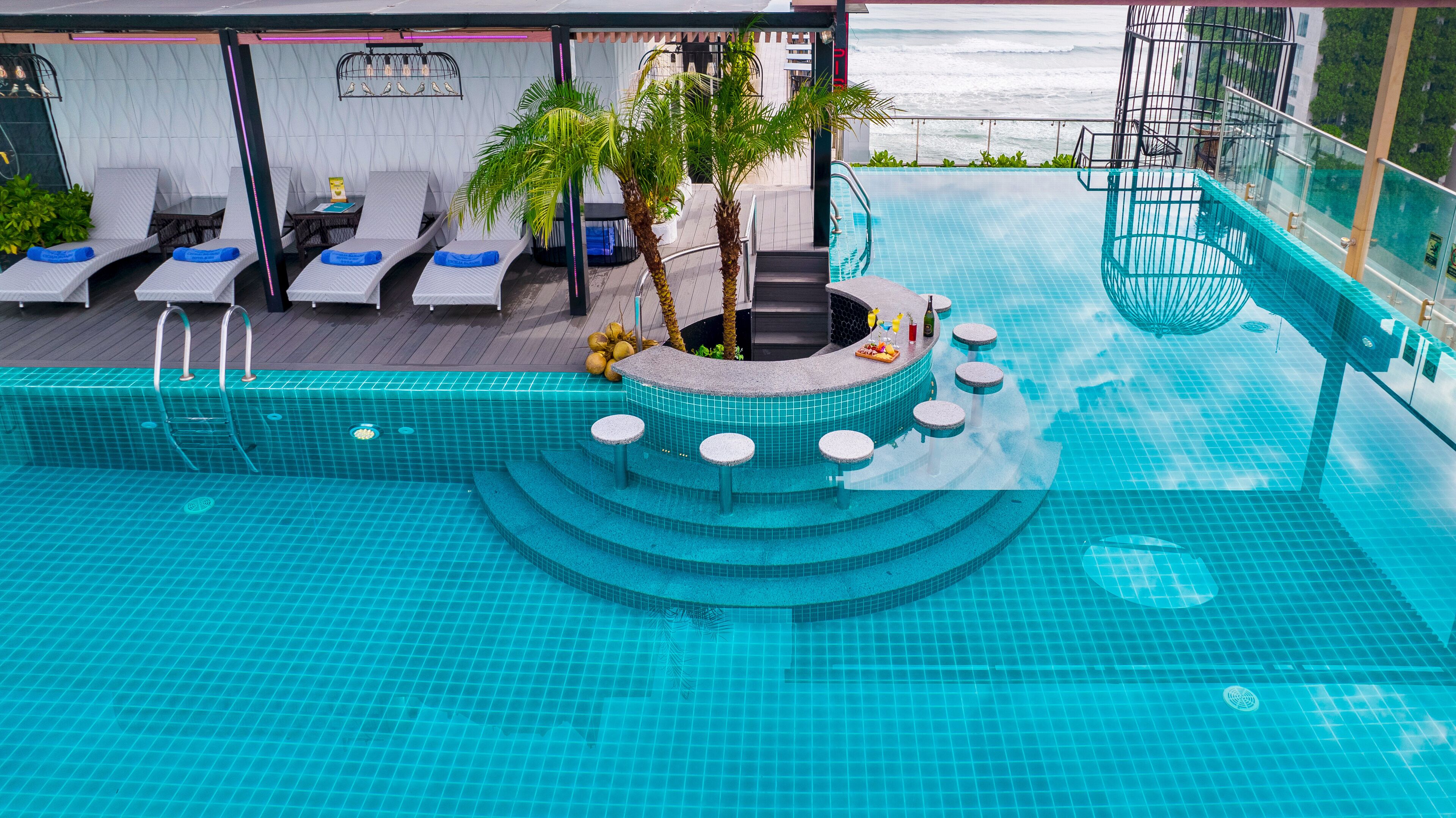 A pool area with lounge chairs, a bar, and a view of the ocean.