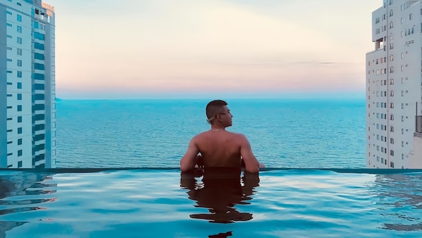 Um homem em uma piscina com vista para o mar e prédios.