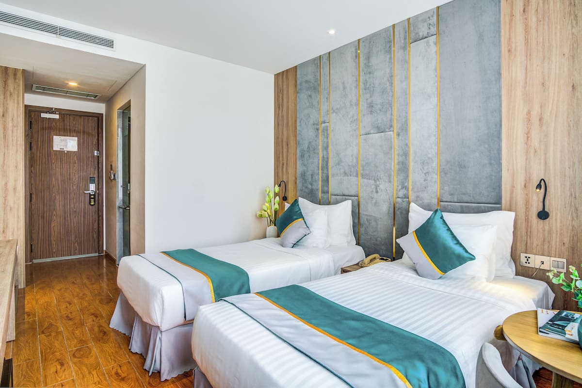 Een hotelkamer met twee bedden, een houten deur, een betonnen accentmuur en een klein tafeltje met een vaas.