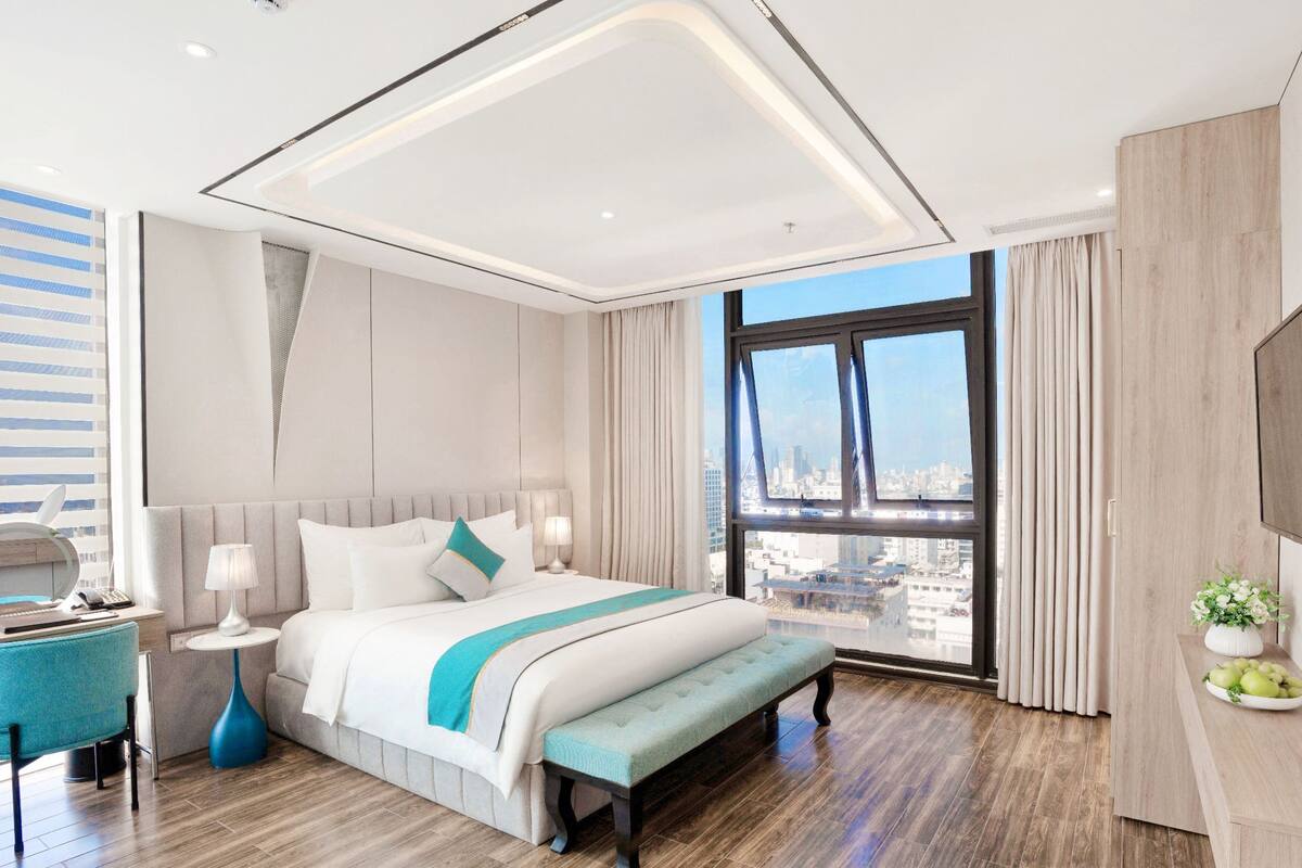 Een moderne hotelkamer met een groot bed, een bureau, een stoel, een bankje, een televisie en uitzicht op de stad.