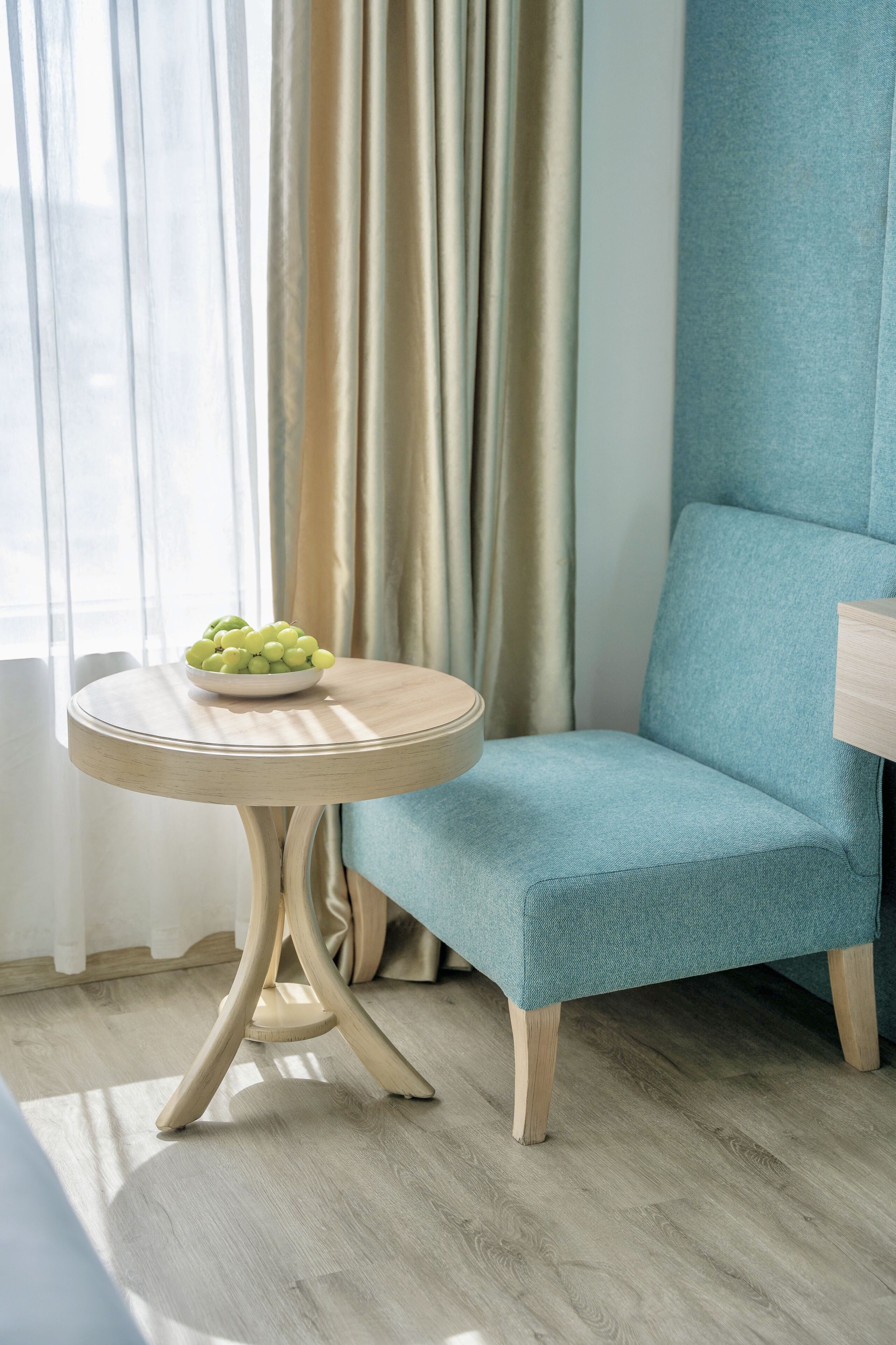 Una habitación con una mesa redonda de madera, una silla tapizada en azul y un cuenco con manzanas verdes.