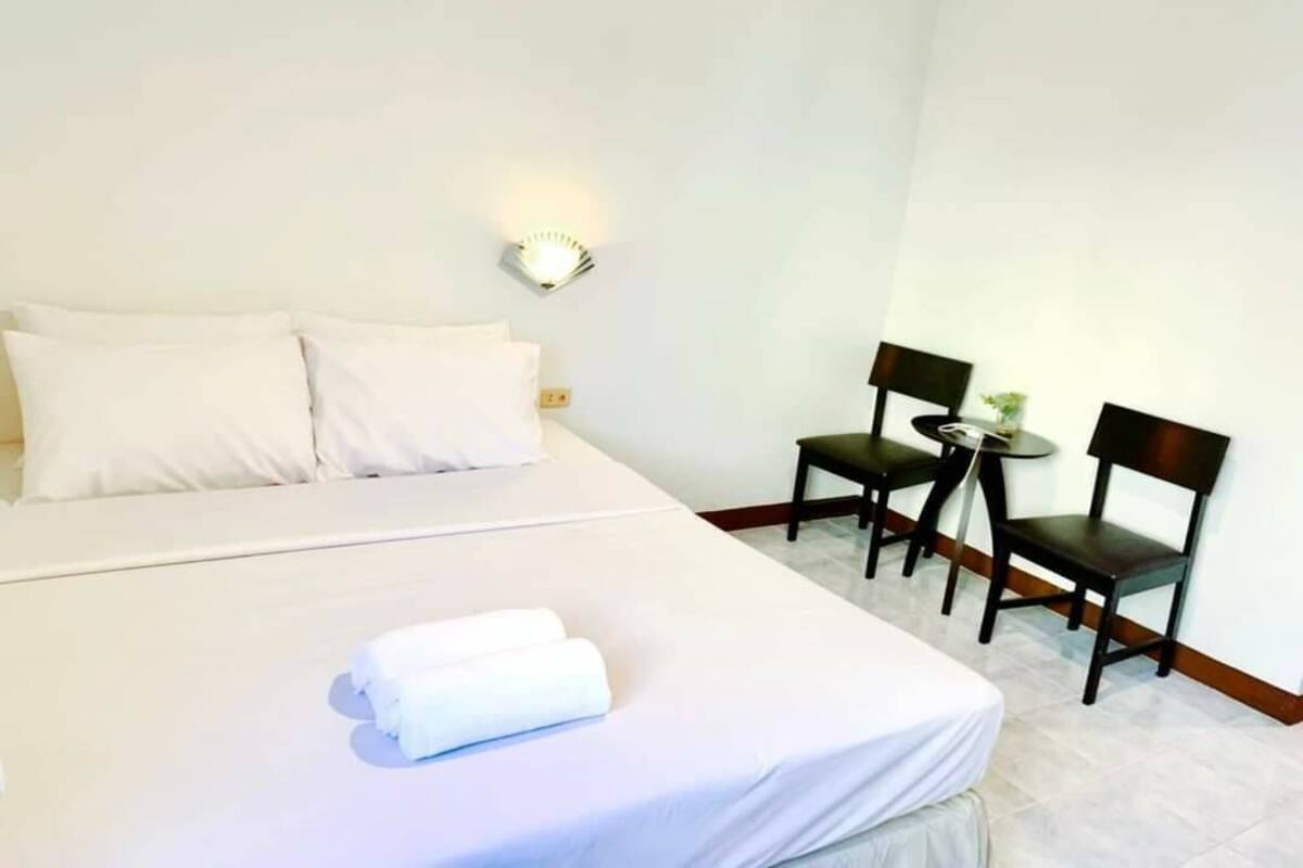 A hotel room with a large bed, two chairs, a small table, and a wall-mounted light fixture.