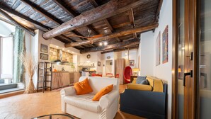 A spacious living area with a white sofa, a blue armchair, and a glass coffee table. A kitchen is visible in the background with a red chair and a dining table. - Orvieto in Terrazza (Orvieto)