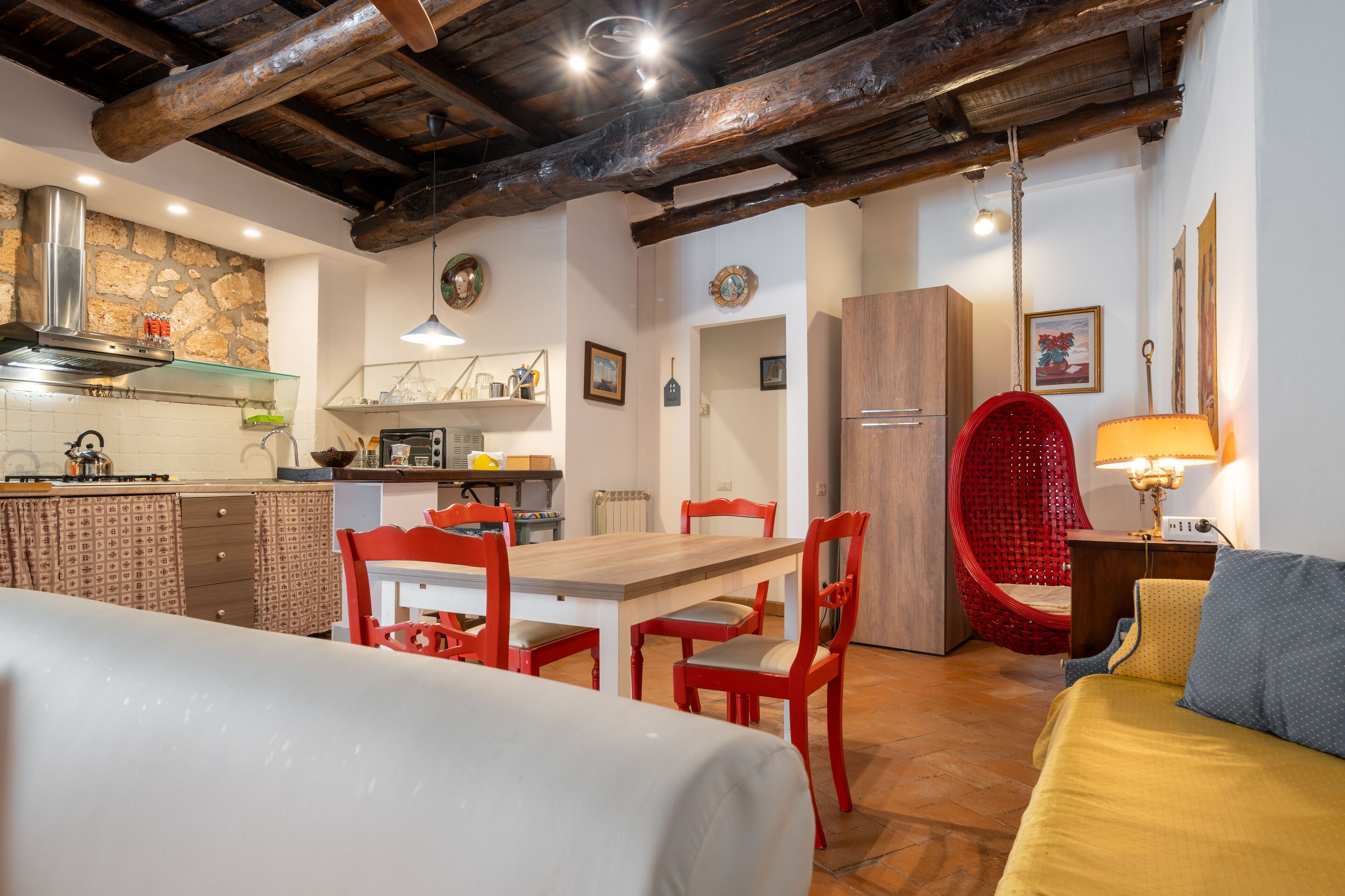Une pièce chaleureuse avec une table à manger en bois, des chaises rouges, un lit et un fauteuil rouge avec un coussin.