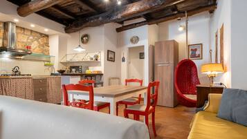Une pièce chaleureuse avec une table à manger en bois, des chaises rouges, un lit et un fauteuil rouge avec un coussin.
