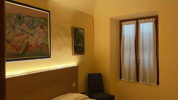 A hotel room with a bed, a chair, a ceiling fan, and two windows with curtains.