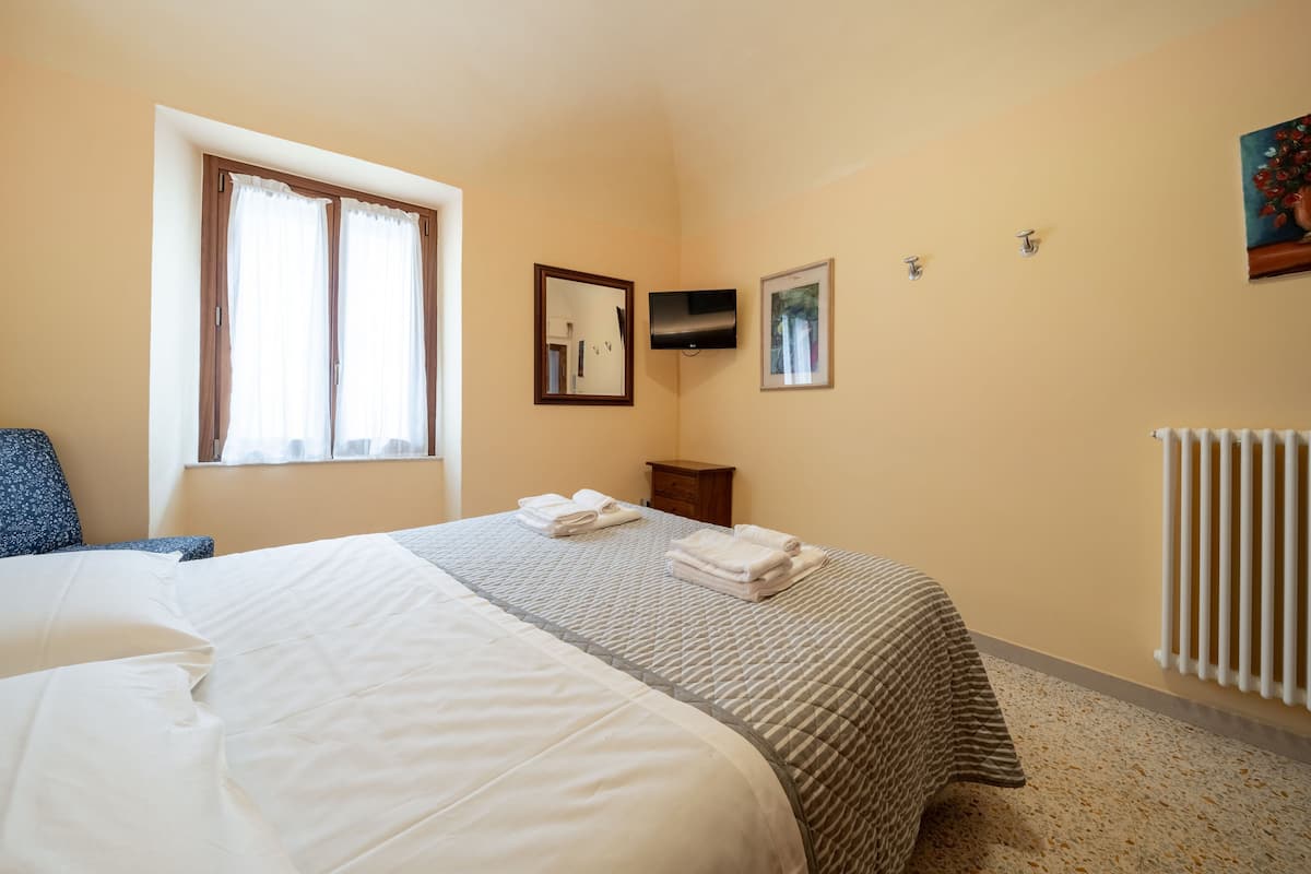 Una camera d'albergo con un letto grande, una finestra con tende, una TV a schermo piatto montata a parete e un termosifone.