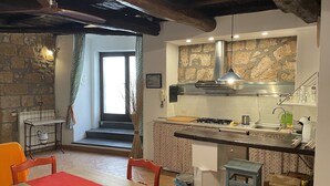 A rustic kitchen with a stone wall, a gas stove, and a wooden dining table with chairs. - Orvieto in Terrazza (Orvieto)