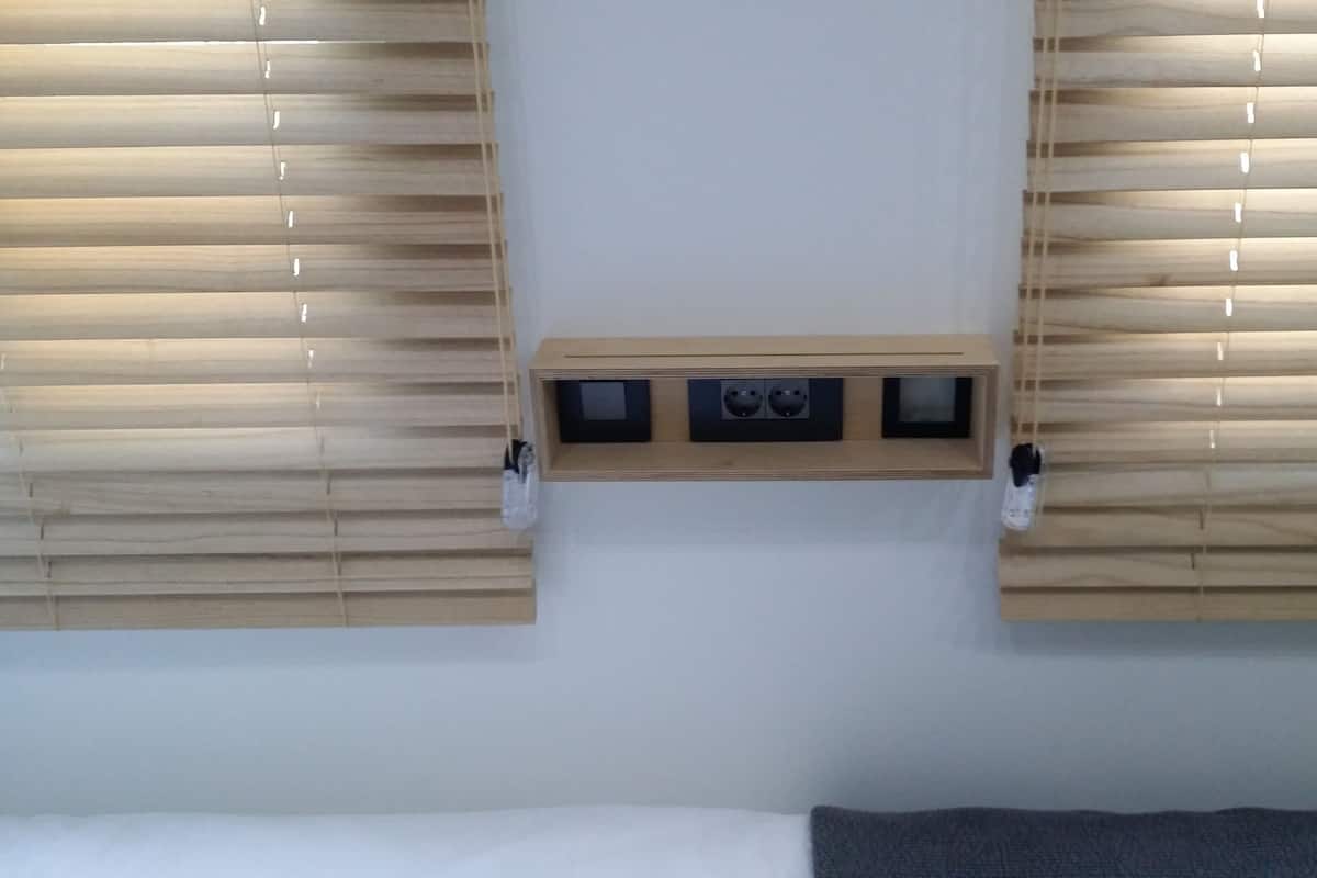 Une chambre à coucher avec un lit, des stores en bois et une prise électrique fixée au mur.