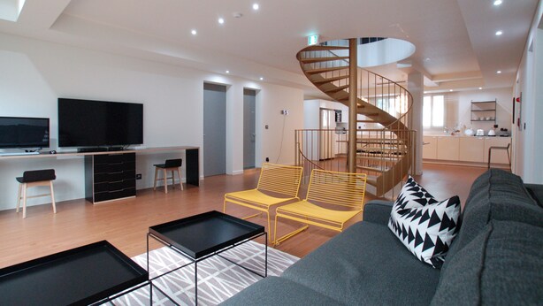 A modern living room with a sofa, a coffee table, and a TV. There is a staircase leading to an upper floor. - YE'4 Guesthouse (Seoul)