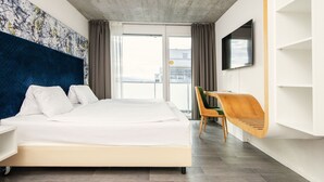 Una habitación de hotel moderna con una cama grande, un televisor montado en la pared y un balcón con vistas.
