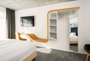 Une chambre d’hôtel moderne équipée d’un lit, d’une chaise en bois, d’un téléviseur fixé au mur et d’une armoire avec un miroir.