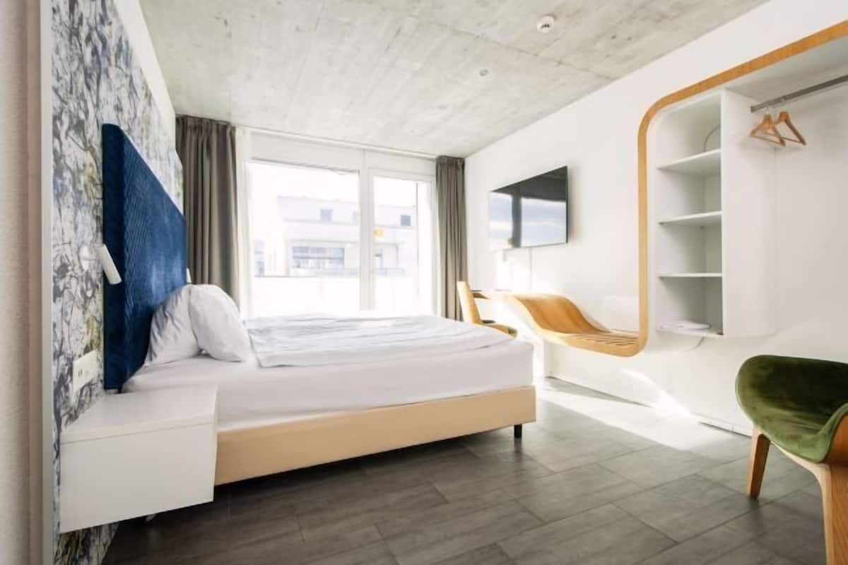 Una habitación de hotel moderna con una cama, una silla, un televisor y un armario.
