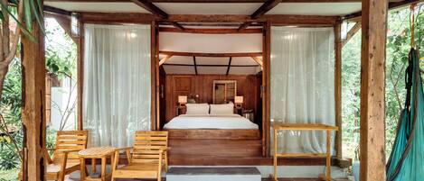A wooden-framed bedroom with a bed, two chairs, a small table, and a bench.