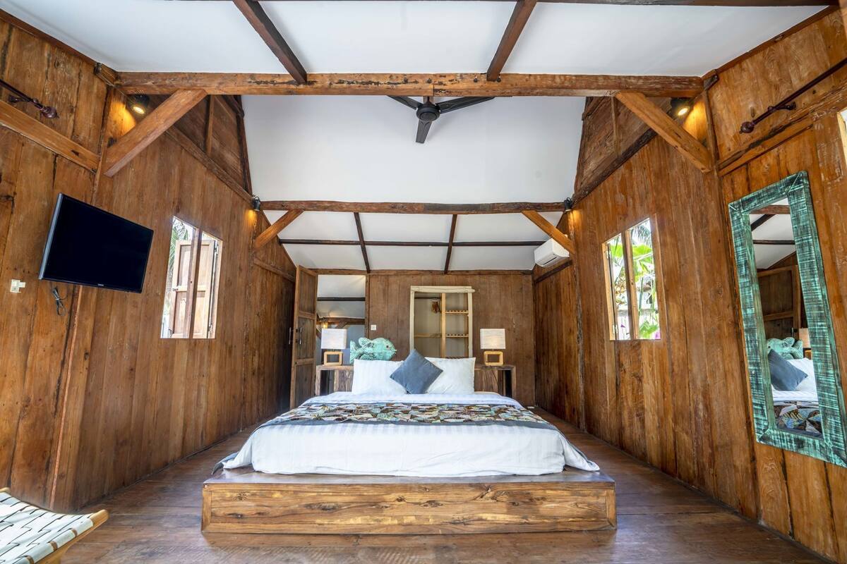 Ein Zimmer mit Holzboden, einem Bett, einem Fernseher und einem Spiegel.