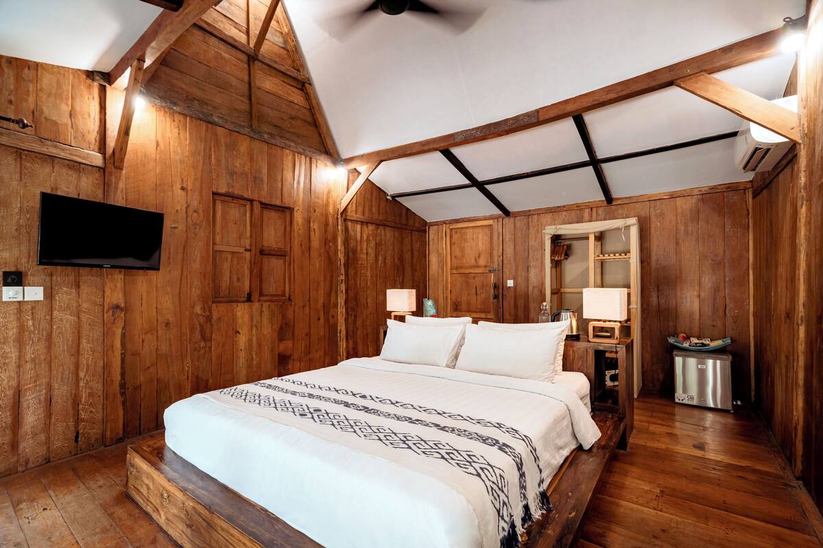 Ein Schlafzimmer mit Holzwänden, einem Bett, einem Flachbildfernseher, einem Spiegel und einem kleinen Tisch mit Lampe.