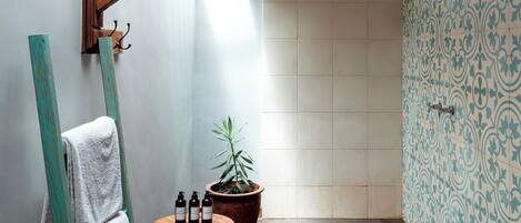 A bathroom with a skylight, wooden beams, a towel rack, a small stool, a potted plant, and patterned tiles.