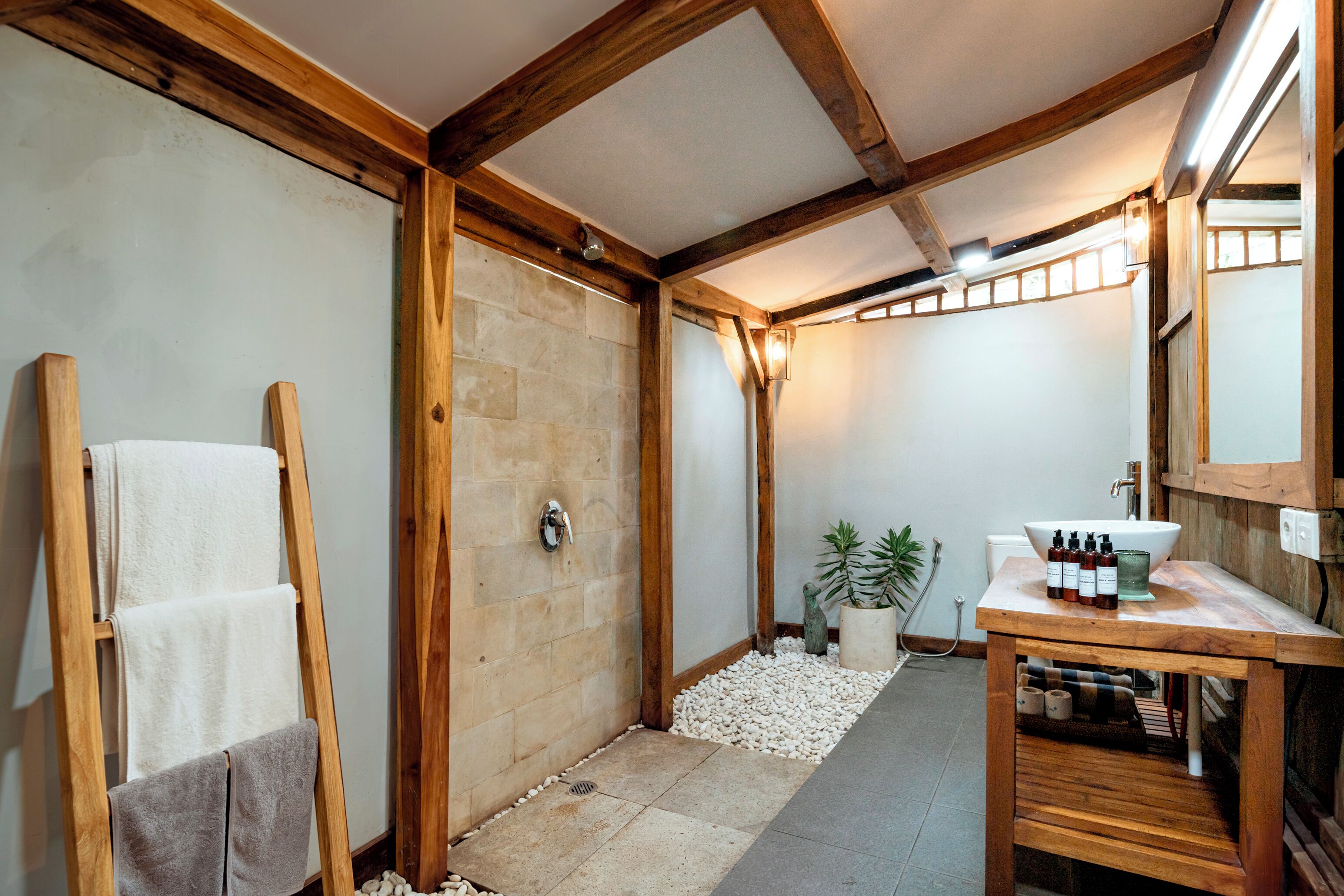A bathroom with a wooden ceiling, a sink, a mirror, and towels on a rack.