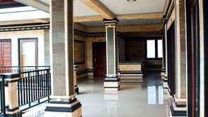 A spacious lobby with high ceilings, polished floors, and a series of columns and doors. - Putu Guest House 2 (Tibubeneng)