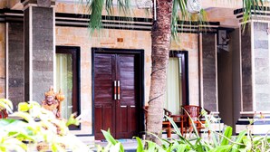 A building with a large wooden door, a statue, and a palm tree. - Putu Guest House 2 (Tibubeneng)