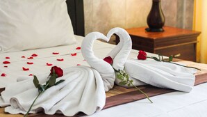 A neatly made bed with white linens, a heart-shaped towel arrangement, and a single red rose. - Putu Guest House 2 (Tibubeneng)